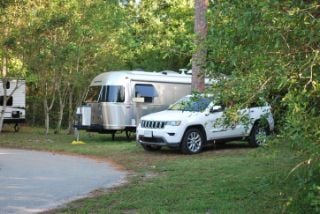 White Jeep and silver Airstream parked under trees.
